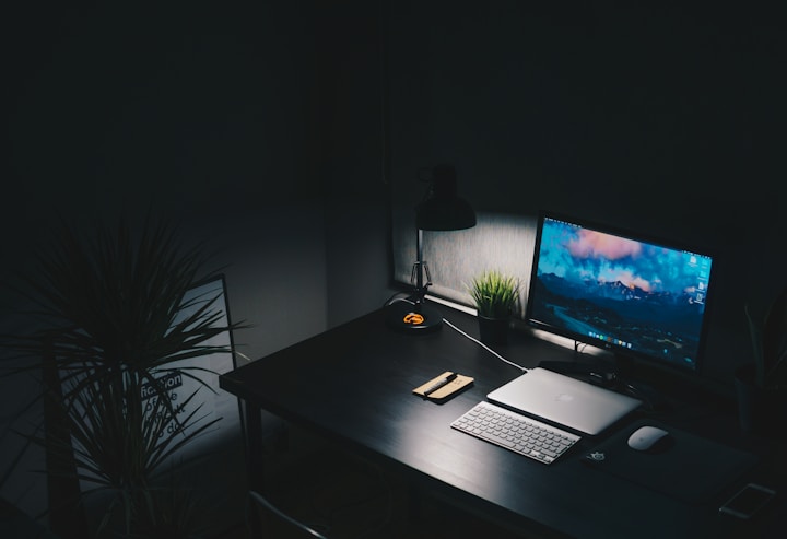 Dark desk at night with a monitor and keyboard lit by a lamp