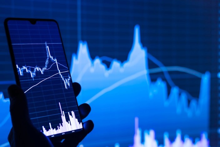 Hand holding a phone with a trading chart on a dark blue screen